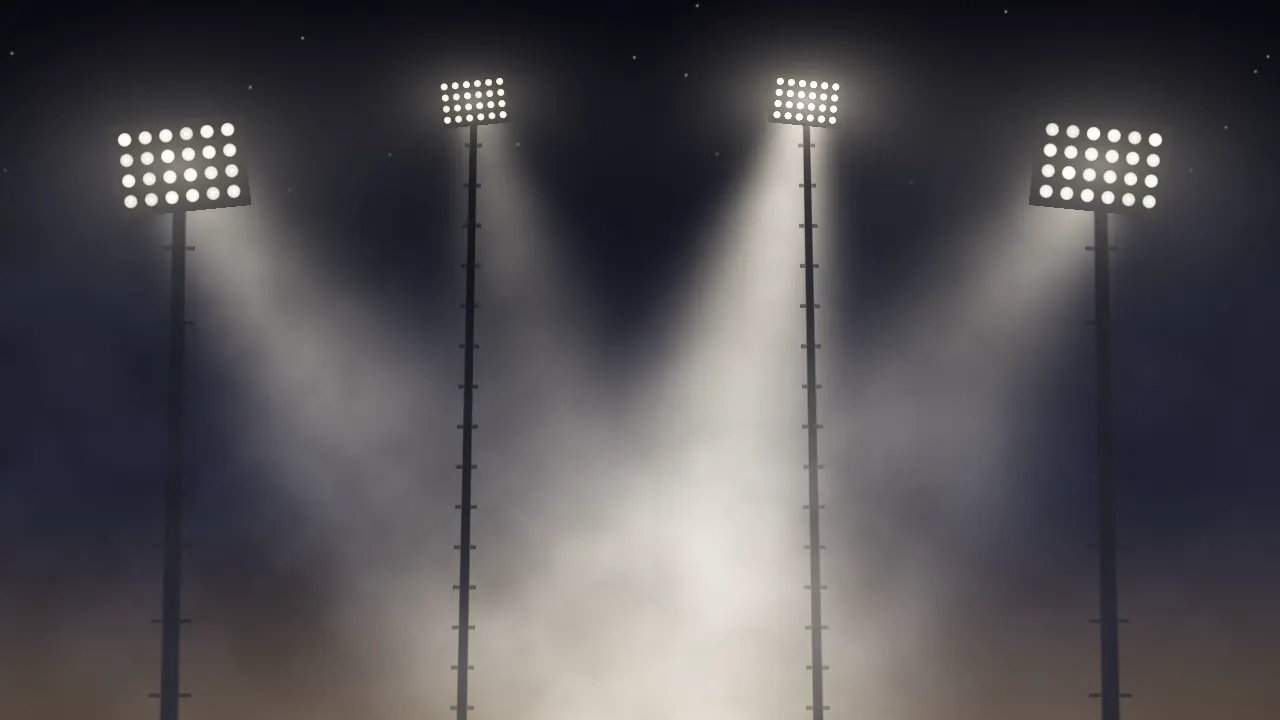Banks of stadium lamps on tall towers seen from below through autumn haze